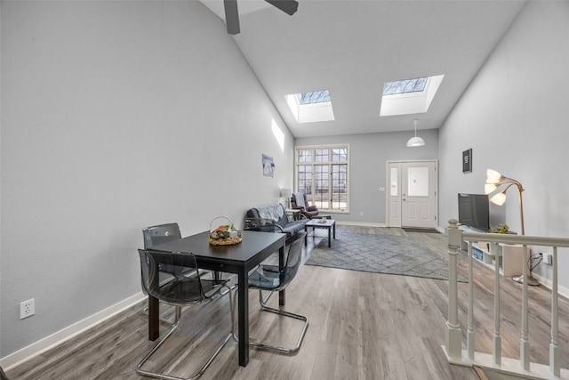 dining space featuring a skylight, wood finished floors, baseboards, and high vaulted ceiling