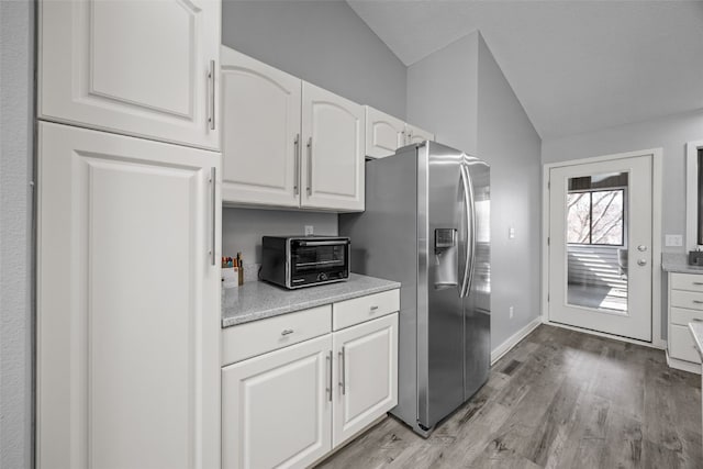 kitchen with light wood-type flooring, lofted ceiling, a toaster, white cabinetry, and stainless steel fridge