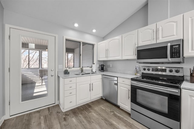 kitchen with light wood finished floors, lofted ceiling, stainless steel appliances, white cabinetry, and a sink