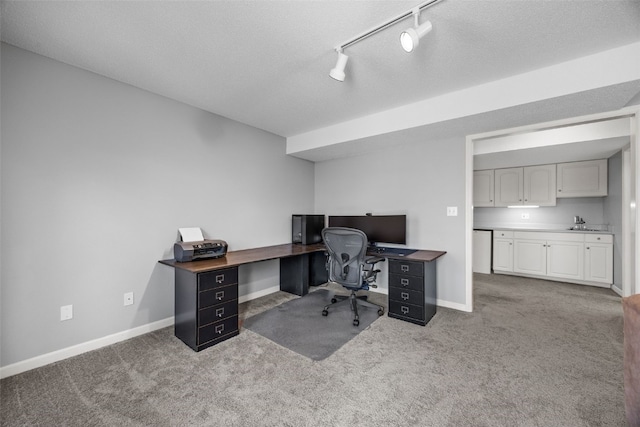 carpeted home office featuring a textured ceiling, track lighting, baseboards, and a sink