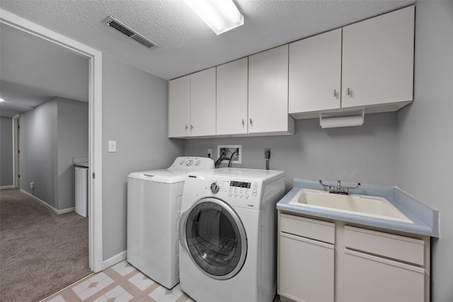 washroom featuring visible vents, washer and dryer, cabinet space, a textured ceiling, and a sink