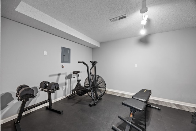 exercise area with electric panel, visible vents, a textured ceiling, and baseboards