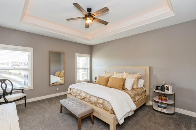 bedroom featuring a raised ceiling, multiple windows, baseboards, and dark carpet