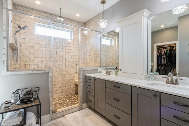 full bathroom featuring double vanity, a stall shower, a walk in closet, and a sink