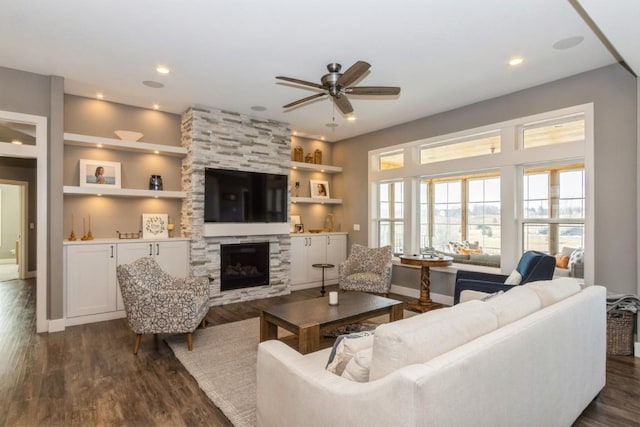 living area featuring dark wood-type flooring, a ceiling fan, built in features, recessed lighting, and a stone fireplace