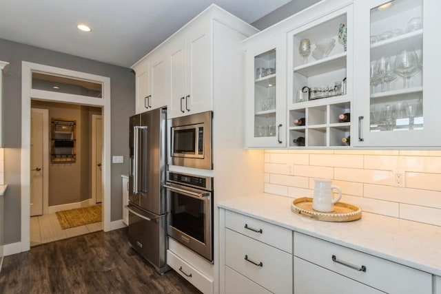 kitchen with light stone counters, dark wood-style floors, white cabinetry, stainless steel appliances, and glass insert cabinets