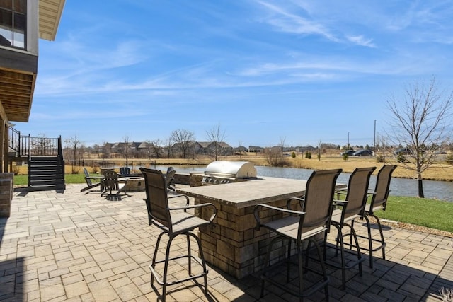 view of patio / terrace with a water view, area for grilling, outdoor wet bar, stairway, and a grill