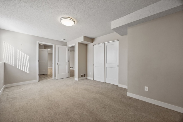 unfurnished bedroom with visible vents, a textured ceiling, a closet, carpet floors, and baseboards