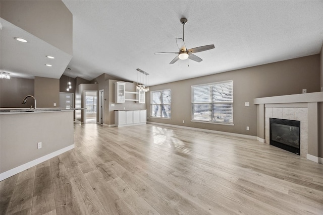 unfurnished living room with a tiled fireplace, vaulted ceiling, ceiling fan with notable chandelier, light wood-style flooring, and a textured ceiling