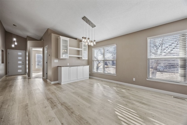 interior space featuring visible vents, light wood-style flooring, open shelves, white cabinets, and lofted ceiling