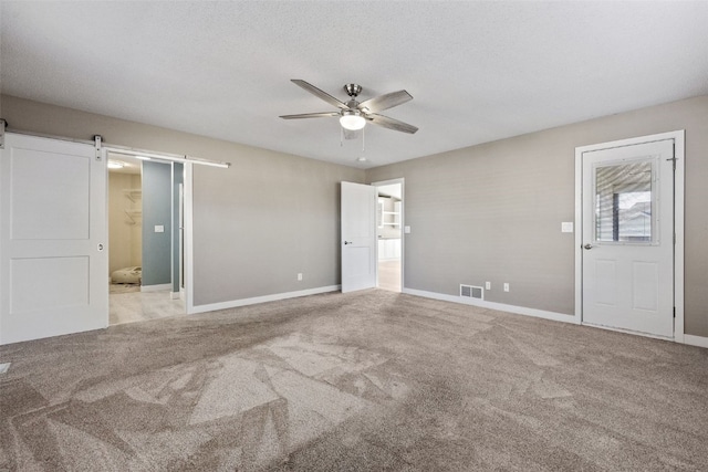 interior space with visible vents, a ceiling fan, a barn door, and carpet floors