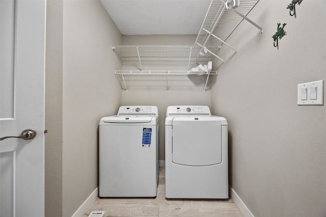 clothes washing area featuring laundry area, independent washer and dryer, light wood-type flooring, and baseboards