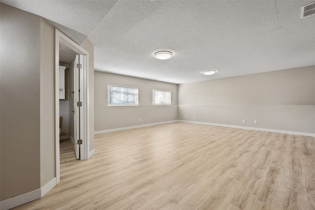 spare room with visible vents, baseboards, light wood finished floors, and a textured ceiling