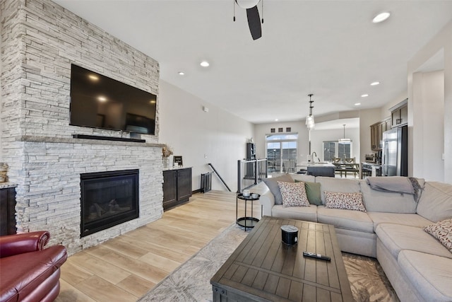 living room featuring recessed lighting, a ceiling fan, a fireplace, and light wood finished floors