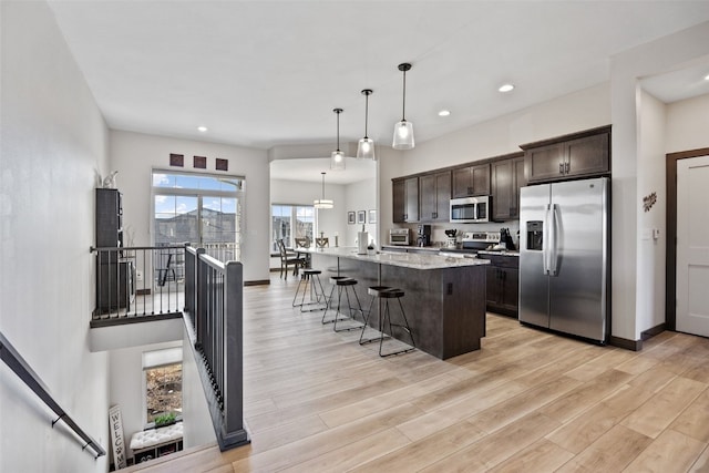 kitchen featuring light stone countertops, light wood finished floors, a breakfast bar, stainless steel appliances, and dark brown cabinets