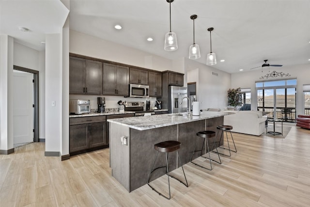 kitchen with a kitchen bar, light wood-style flooring, open floor plan, stainless steel appliances, and dark brown cabinets