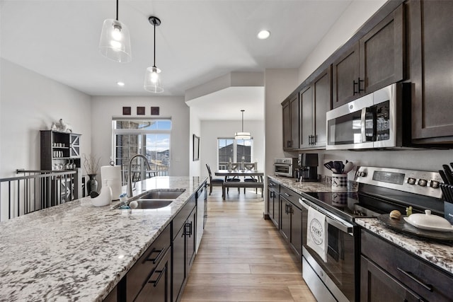 kitchen featuring dark brown cabinets, light stone countertops, light wood-type flooring, stainless steel appliances, and a sink