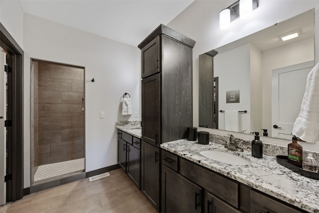 bathroom featuring tiled shower, vanity, and baseboards