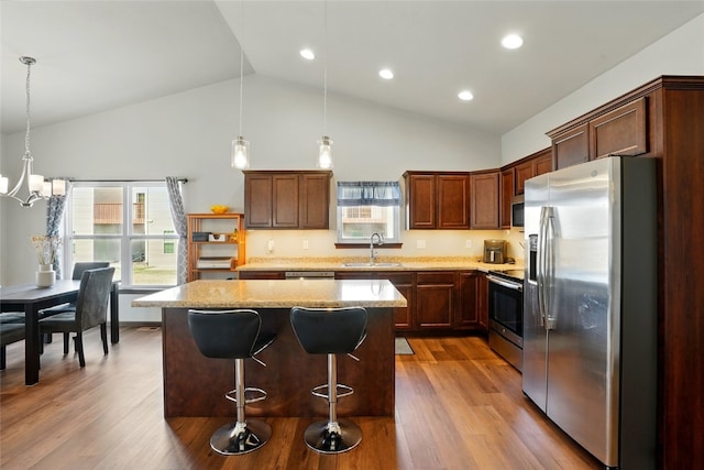 kitchen with wood finished floors, a kitchen island, a sink, stainless steel appliances, and decorative light fixtures