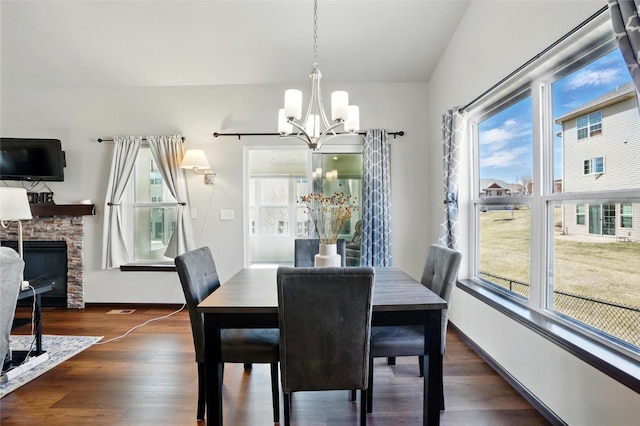 dining area featuring dark wood-style floors, a stone fireplace, baseboards, and an inviting chandelier