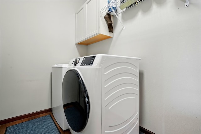 laundry room featuring baseboards, cabinet space, wood finished floors, and washing machine and clothes dryer