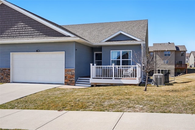 view of front of property featuring driveway, stone siding, an attached garage, a front yard, and central AC unit