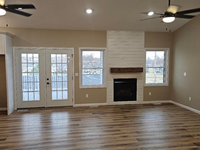 unfurnished living room with french doors, a large fireplace, ceiling fan, and dark wood finished floors