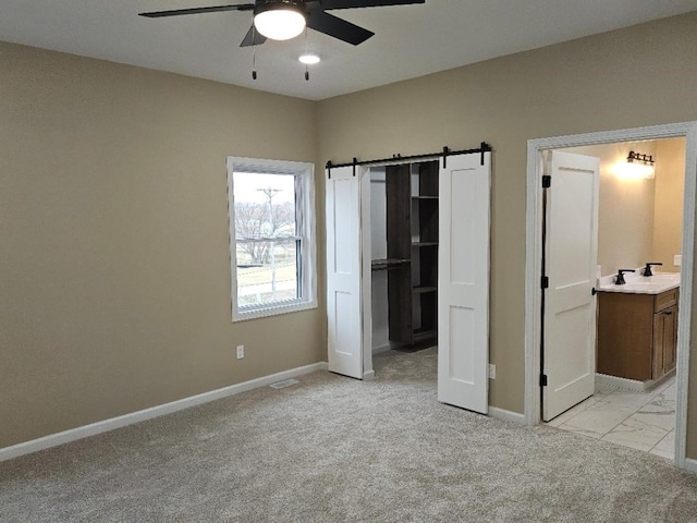 unfurnished bedroom featuring a barn door, baseboards, ensuite bathroom, and light carpet