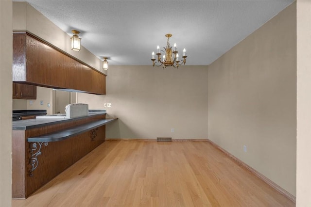 kitchen with dark countertops, a chandelier, brown cabinets, light wood-style floors, and a textured ceiling