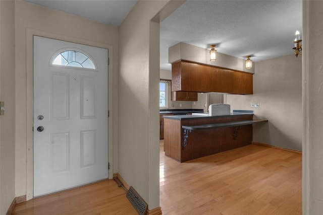 kitchen featuring dark countertops, visible vents, light wood-type flooring, brown cabinets, and a peninsula