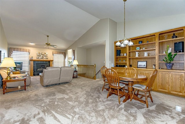 carpeted dining room with a tiled fireplace, ceiling fan with notable chandelier, and high vaulted ceiling