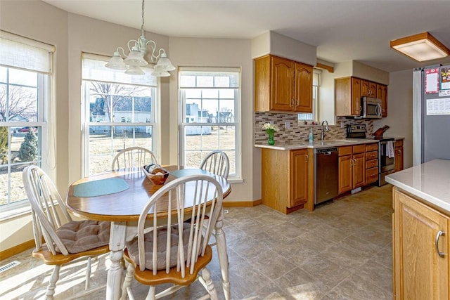 kitchen featuring backsplash, light countertops, a wealth of natural light, an inviting chandelier, and stainless steel appliances