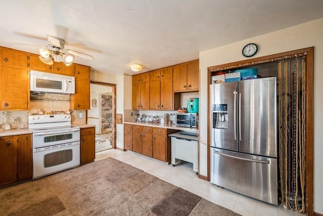 kitchen featuring tasteful backsplash, light countertops, brown cabinets, white appliances, and a ceiling fan