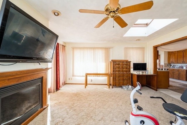 workout area featuring a ceiling fan, a glass covered fireplace, carpet, a skylight, and baseboards