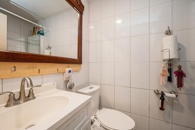 bathroom with toilet, vanity, tile walls, and a shower