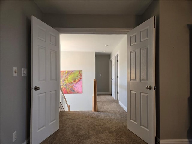 corridor with baseboards, an upstairs landing, and carpet floors