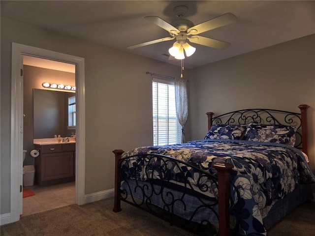 bedroom featuring baseboards, ensuite bath, a sink, ceiling fan, and light colored carpet