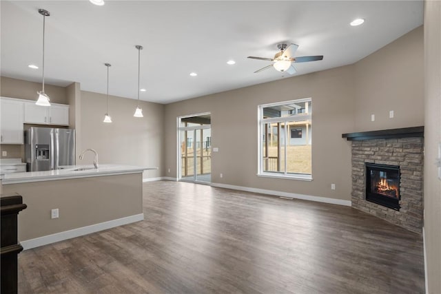 unfurnished living room with dark wood-type flooring, a sink, a fireplace, baseboards, and ceiling fan