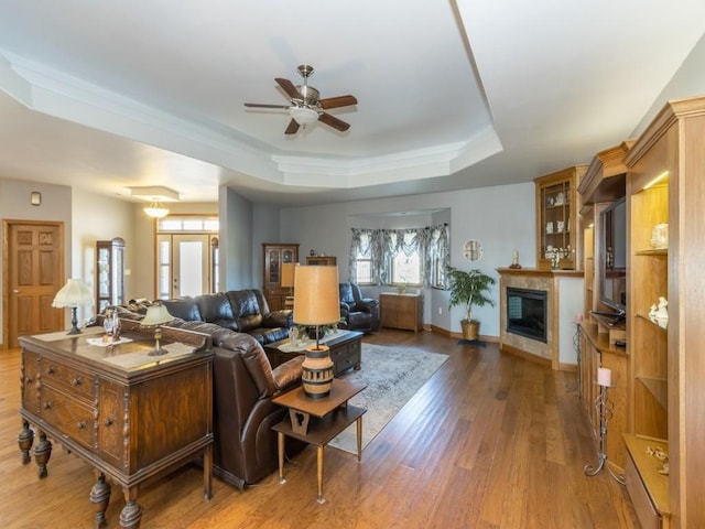 living area with baseboards, ceiling fan, wood finished floors, a glass covered fireplace, and a raised ceiling