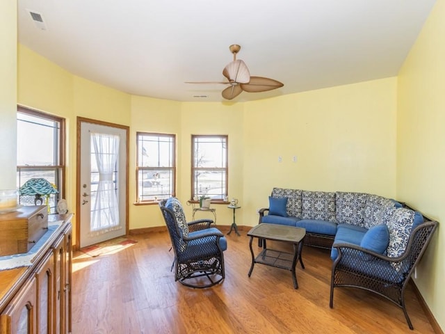 living room with light wood-style flooring, a ceiling fan, visible vents, and baseboards