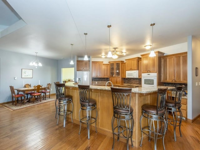 kitchen with decorative backsplash, white appliances, light wood-style flooring, and brown cabinets