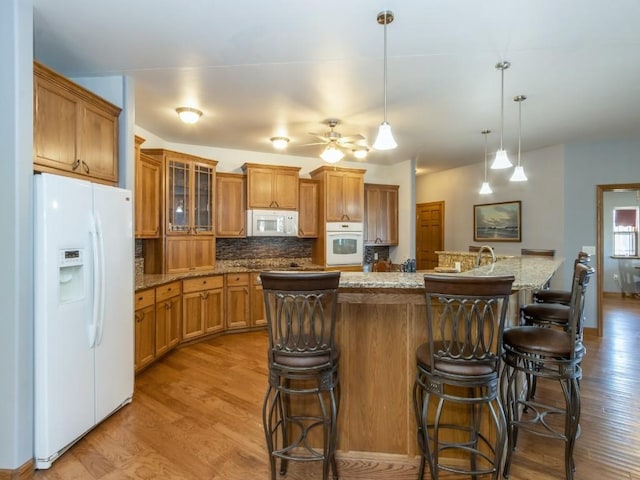 kitchen featuring backsplash, wood finished floors, white appliances, brown cabinetry, and ceiling fan