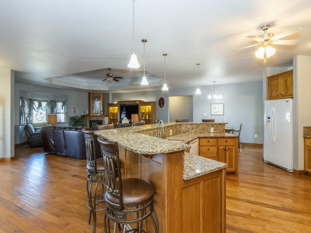 kitchen with open floor plan, a tray ceiling, light wood-style floors, white appliances, and a ceiling fan