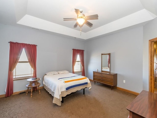 carpeted bedroom with a tray ceiling, visible vents, baseboards, and ceiling fan