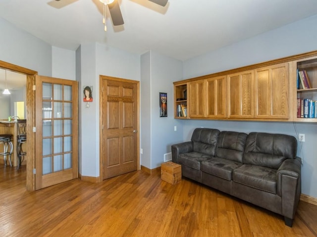 living area featuring visible vents, a ceiling fan, baseboards, and light wood finished floors