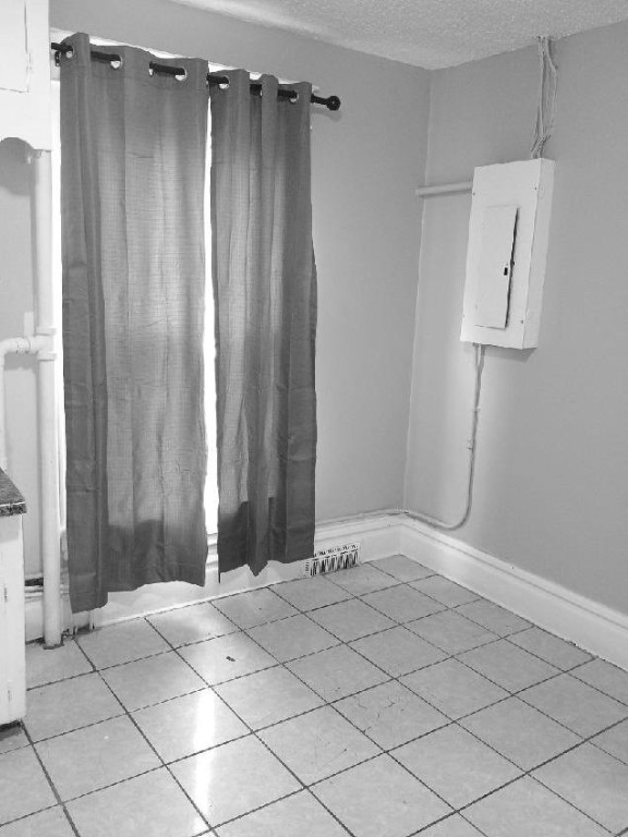 spare room featuring electric panel, light tile patterned flooring, and a textured ceiling