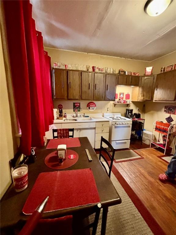 kitchen with a sink, dark wood-style flooring, white gas range, and light countertops