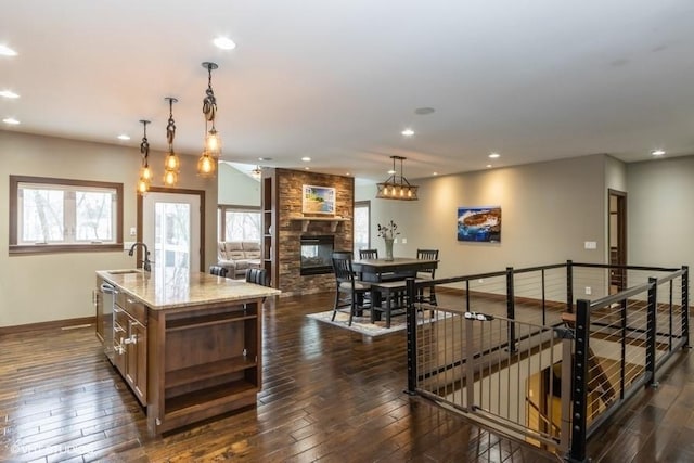 kitchen with an island with sink, light stone countertops, dark wood-style flooring, and a sink