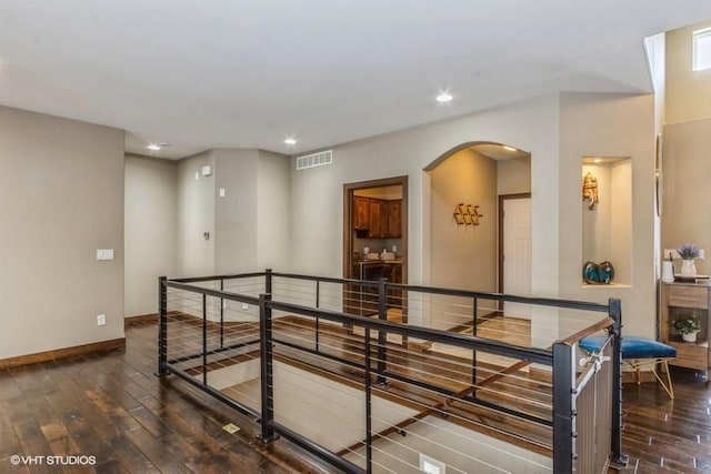 hall with hardwood / wood-style floors, baseboards, visible vents, arched walkways, and an upstairs landing