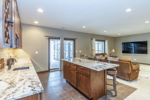 kitchen with a kitchen bar, a sink, a kitchen island, recessed lighting, and light stone countertops